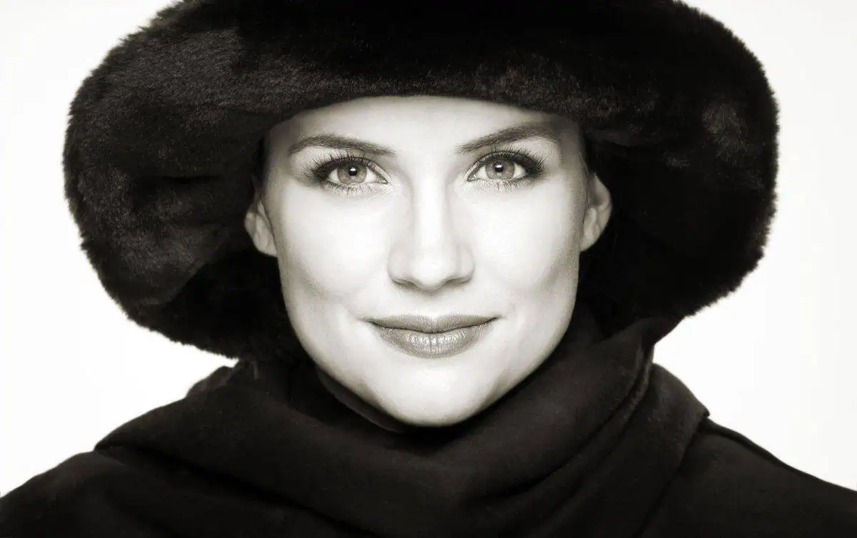A woman, her modeling portfolio brought to life, dons a large fur hat and coat. She stares directly at the camera with a neutral expression in this striking black and white image.