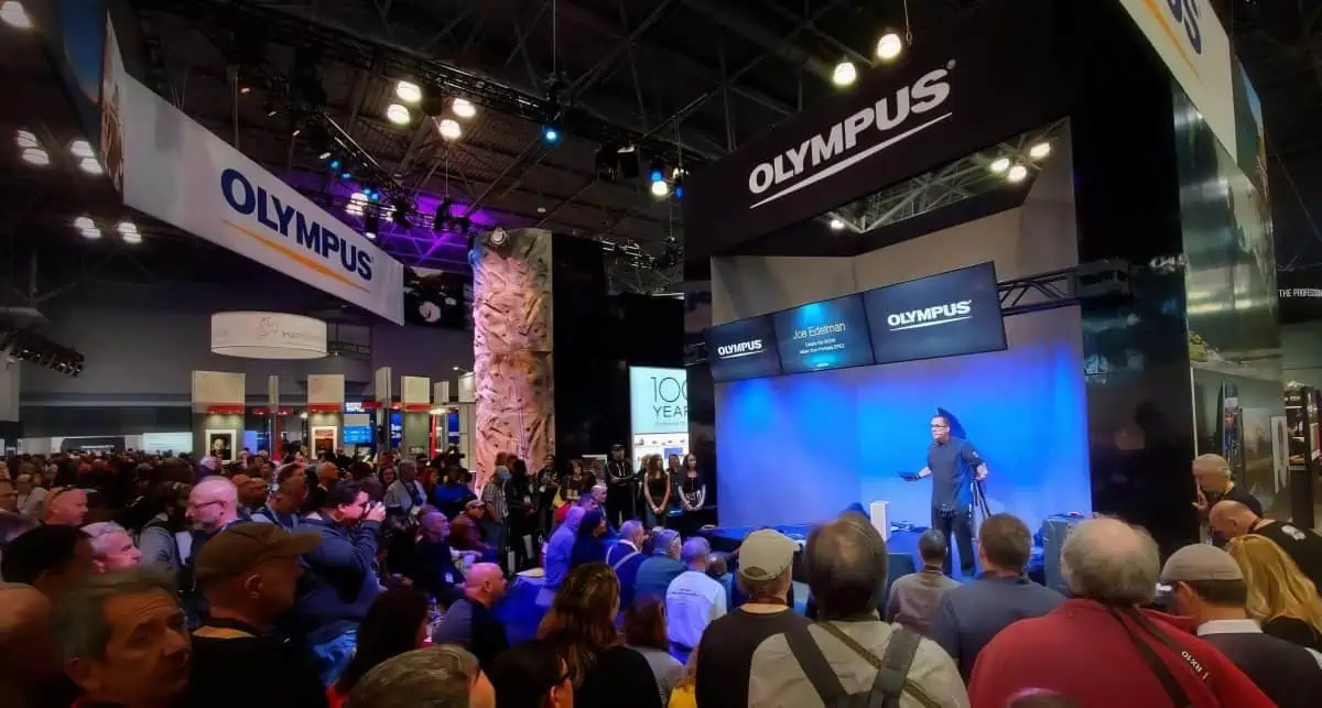 Joe Edelman on stage at PhotoPlus with a crowd of people.
