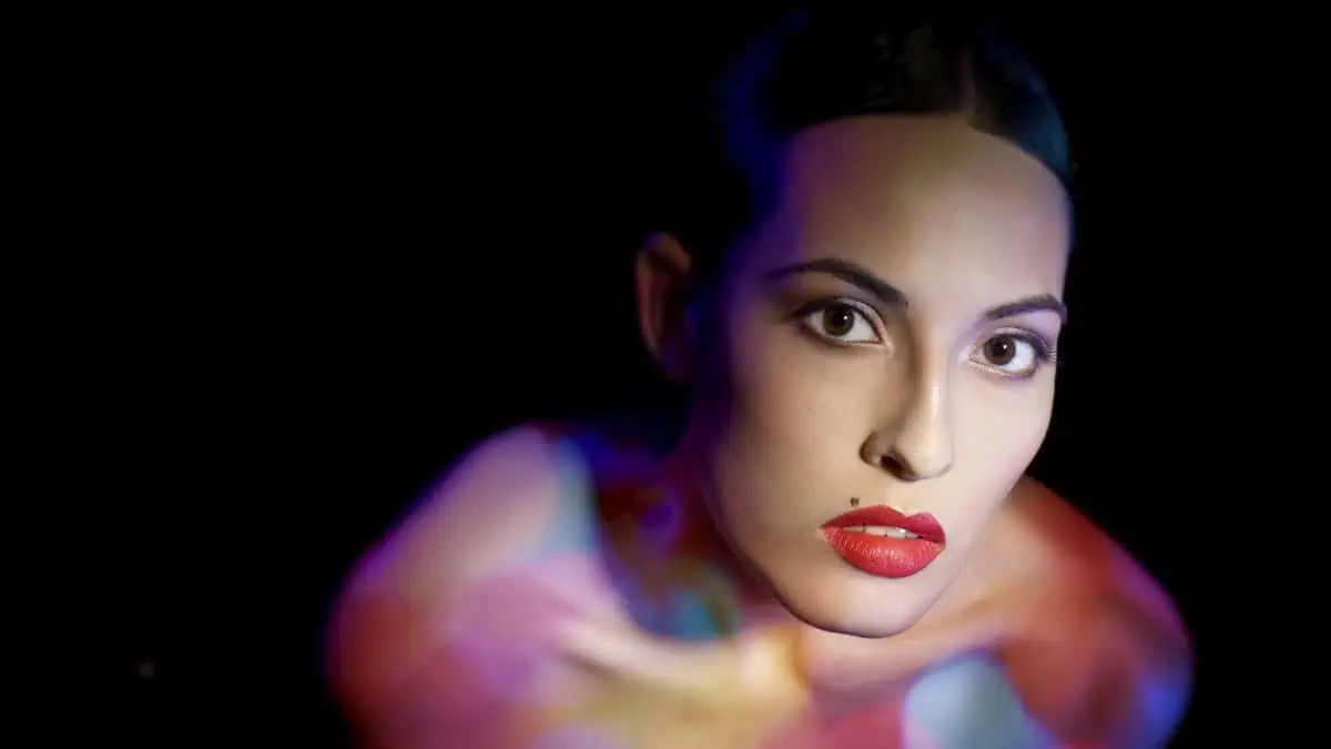 A woman with a brightly colored body is posing in front of a dark background.