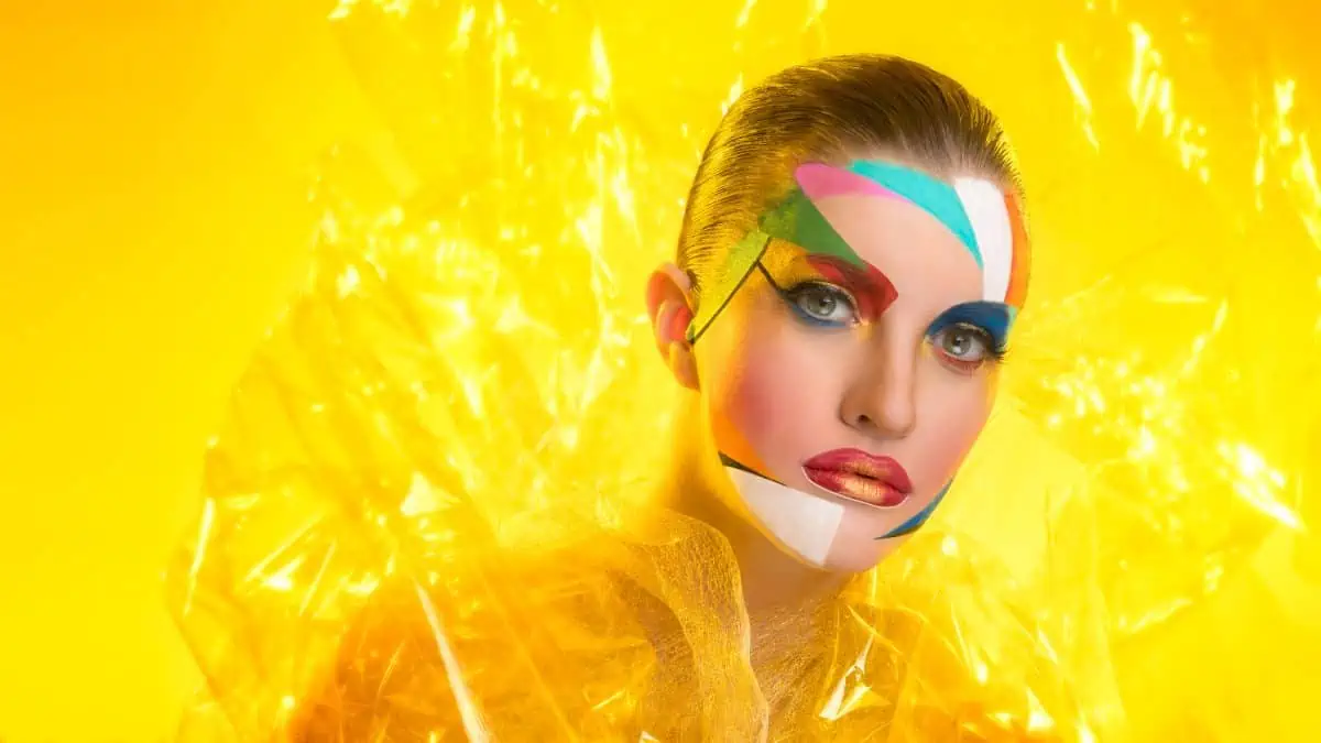 A woman with colorful face paint on a yellow background.