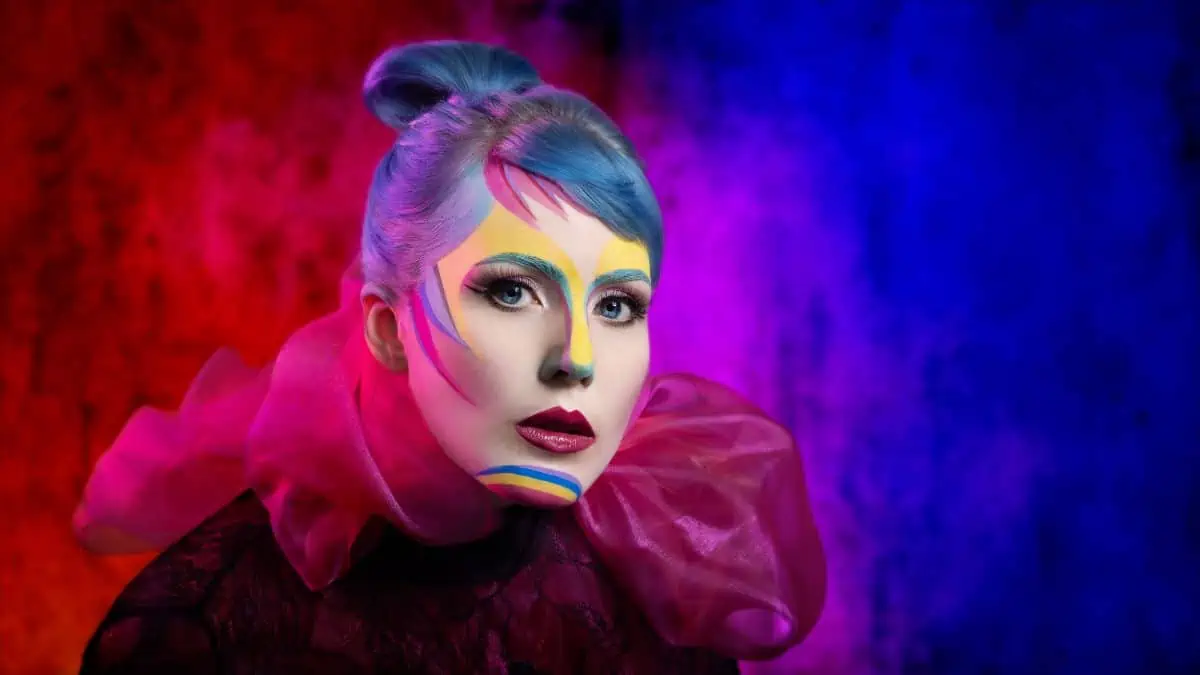A woman with colorful makeup in front of a colorful background.