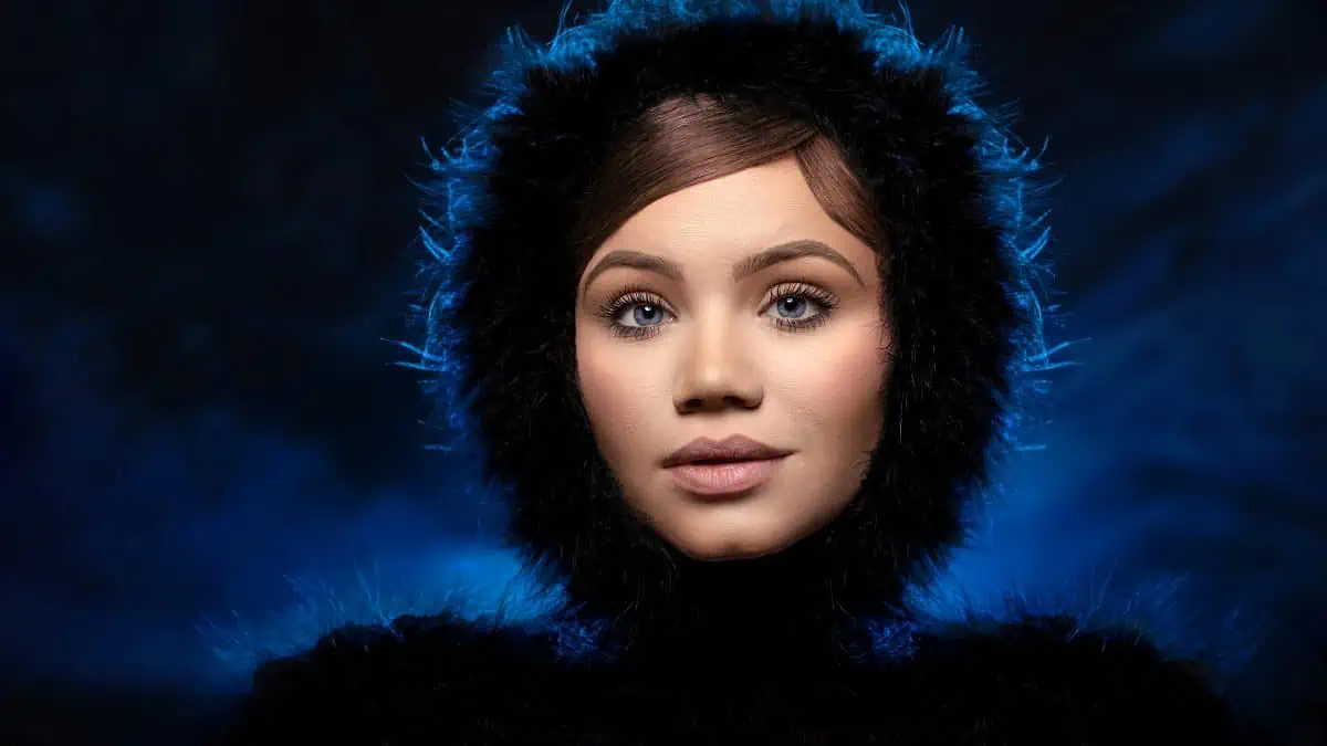 A woman in a fur coat is posing in front of a blue background.
