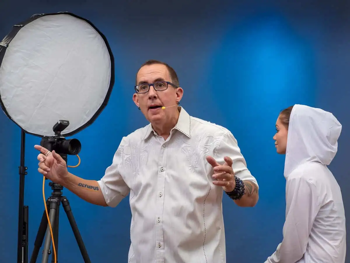A man in a white shirt standing next to a light stand.