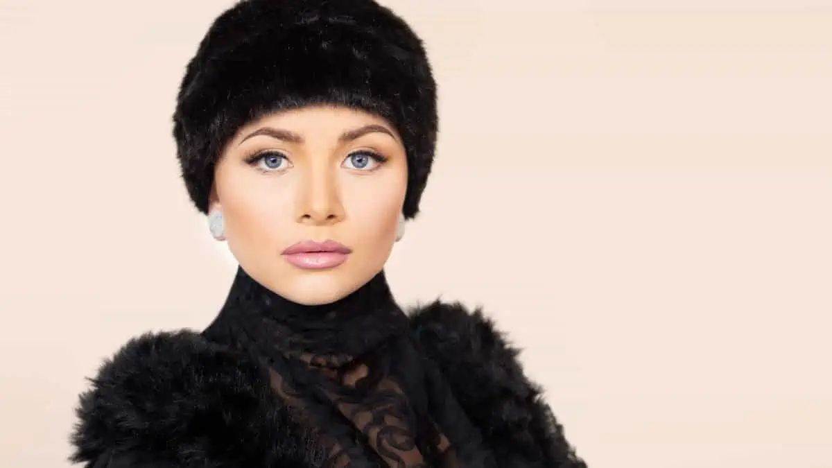 A woman in a black fur hat posing on a beige background.
