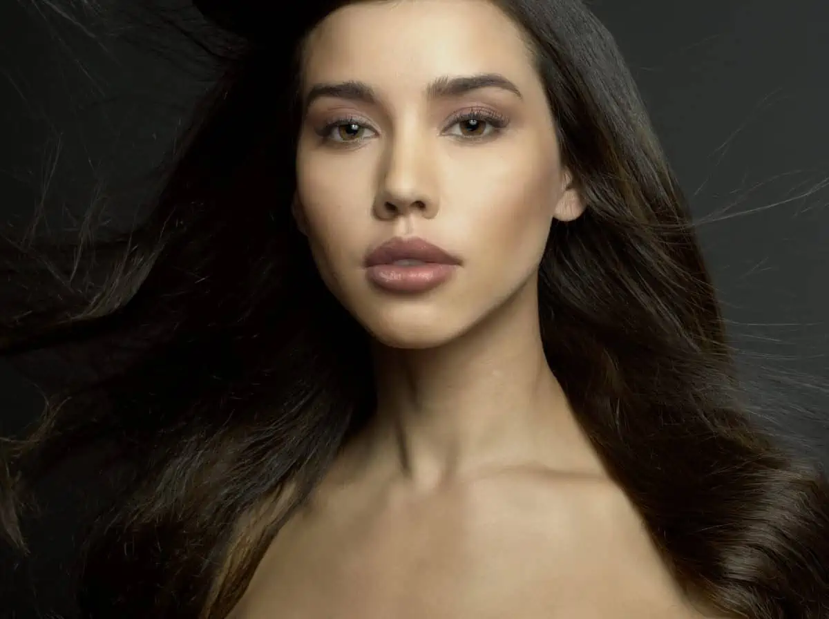 A young woman with long hair posing on a dark background.