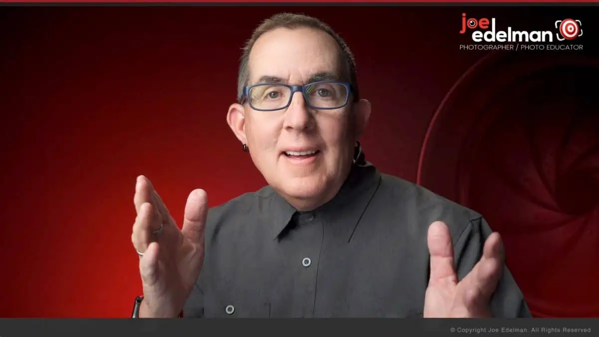 A man in glasses is standing in front of a red background.