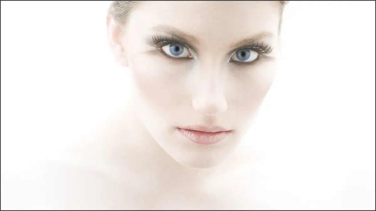 A woman with blue eyes is posing for a photo, illuminated by beauty lighting.
