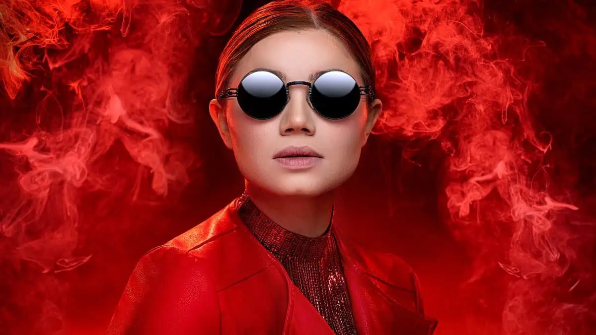 A woman wearing red sunglasses stands in front of a smoke machine, creating a mesmerizing ambiance.