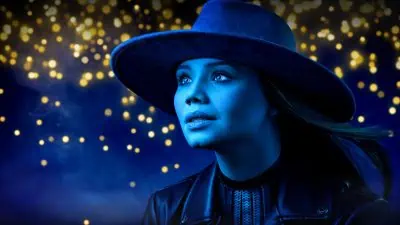 A woman wearing a blue hat poses gracefully in front of vibrant blue lights, creating a captivating and colorful beauty portrait.