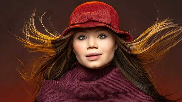 A creatively beautiful woman wearing a red hat and scarf poses for a portrait.