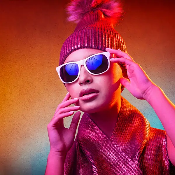 A creatively styled woman wearing sunglasses and a beanie, captured in a beauty portrait.