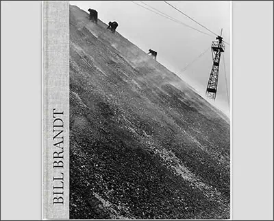 Black and white photograph of a steep slope with industrial machinery at the top and a tall utility pole on the right. The cover reads "Bill Brandt" on the left side.