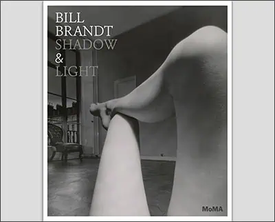 Black and white photograph of a person's legs stretched out in a room with a chair and window in the background. Text reads: "Bill Brandt Shadow & Light, MoMA.