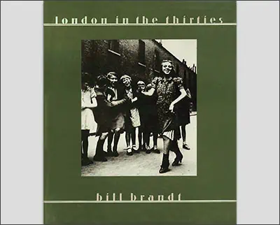 Cover of the book "London in the Thirties" by Bill Brandt, featuring a black and white photo of children playing in the street with a green border and white text.