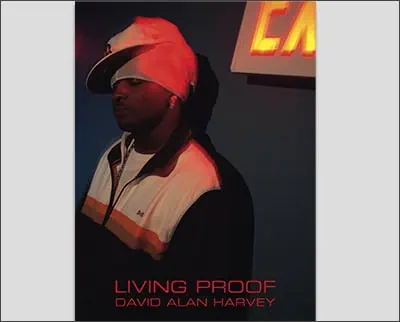 A person wearing a cap, hoodie, and jacket stands near a red illuminated sign in a dark environment. Text on the image reads "Living Proof David Alan Harvey," evoking the striking style reminiscent of Joe McNally's work.