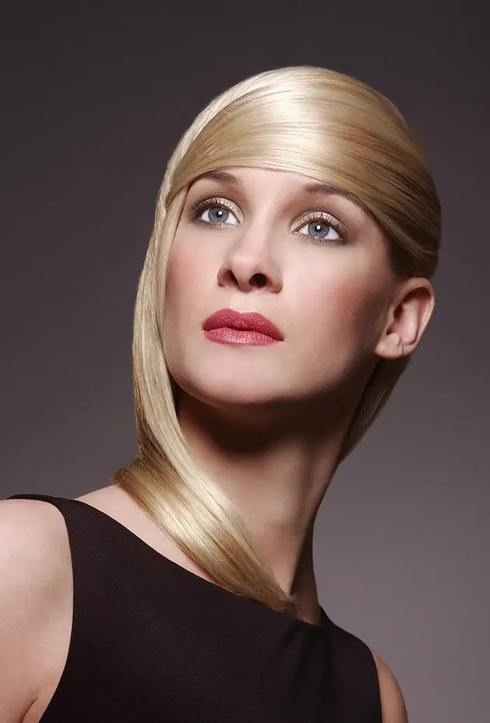 With long, sleek blonde hair styled elegantly around the head and a black top accentuating her poise, she gazes upward against a dark backdrop—a perfect embodiment of classic modeling terms.
