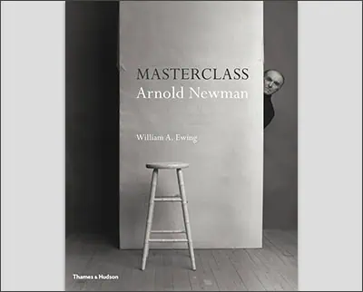 Cover of "Masterclass: Arnold Newman" by William A. Ewing, featuring a photograph reminiscent of Margaret Bourke-White's style with a wooden stool and a person peeking from behind a large board with the book’s title. Published by Thames & Hudson.
