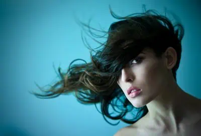 A woman with long hair blowing across her face against a blue background.