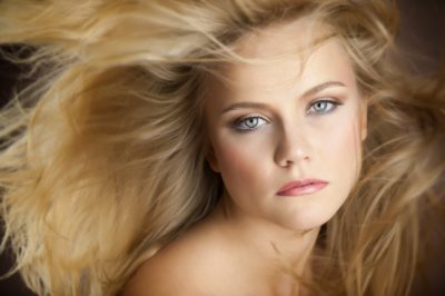 A person with long, flowing blonde hair and a neutral expression looks directly at the camera.
