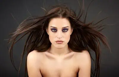 Woman with long brown hair and bold makeup, against a dark background.