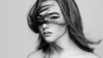 Black and white photo of a person with straight hair blown across their face, looking directly at the camera.