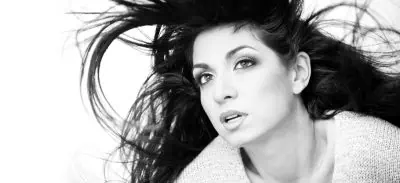 Black and white close-up of a woman with long hair flowing around her face, looking upwards.