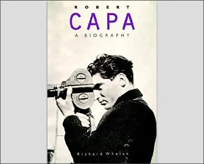 Book cover titled "Robert Capa: A Biography" by Richard Whelan, showcasing an image of the legendary war photographer capturing life's intense moments with his camera.