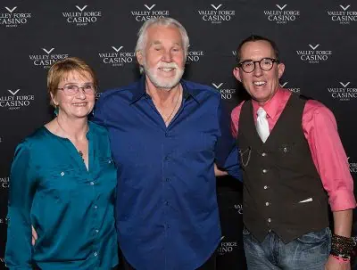 Three people stand smiling in front of a backdrop for Valley Forge Casino Resort.