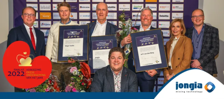 Seven people stand smiling in front of a sponsor wall, holding framed certificates and flowers. A badge reads “Finalist 2022 Verkiezing Friese Onderneming van het Jaar.” The Jongia Mixing Technology logo appears at the bottom right.