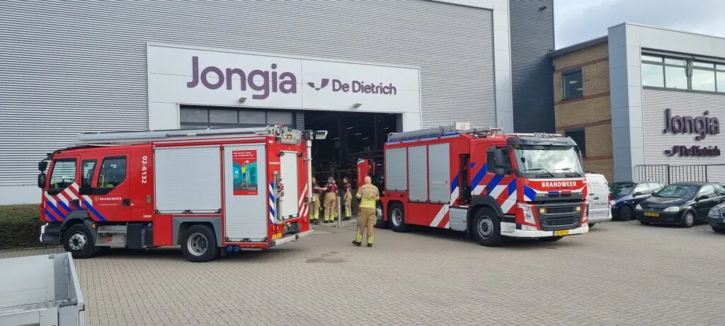 Two fire engines parked outside the Jongia De Dietrich building during Safety Day, with firefighters walking into the production hall.