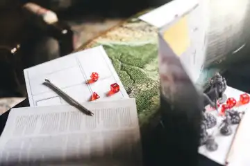 Auf einem Tisch steht ein Spielleiterschirm neben Würfeln und Figuren für den Tabletop RPG Game Master.