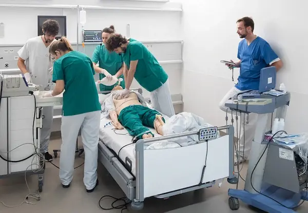 Medical team in scrubs performing emergency simulation with defibrillator on mannequin in hospital training room.
