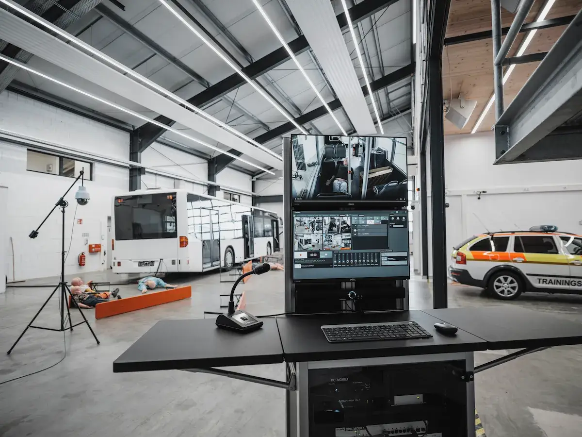 A contemporary debriefing room equipped with ergonomic tablet-arm chairs and a large wall-mounted interactive screen for reviewing recorded medical simulation data.