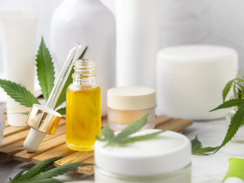 Dropper bottle with CBD oil and cream bottles green cannabis leaves close up in bathroom. Organic healthcare product. Alternative medicine for sleep and relax, CBD cosmetics