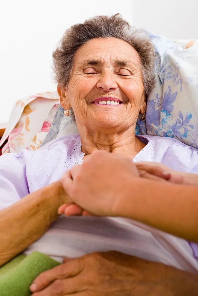 Caring nurse holding kind elderly lady's hands in bed.