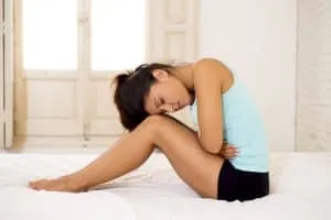 young beautiful hispanic woman in painful expression holding her belly suffering menstrual period pain lying sad on home bed having tummy cramp in female health concept