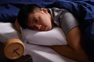 A depressed young man suffering from insomnia lying in bed