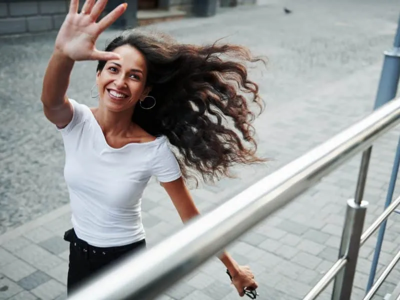 Happy to see you. Beautiful woman with curly black hair have good time in the city at daytime.