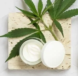 opened cream jar with leaf cannabis