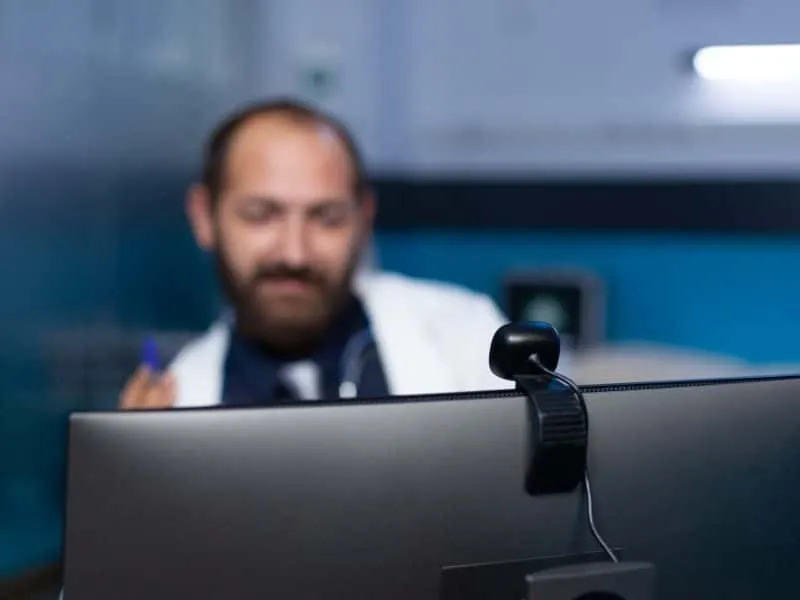 Close up of webcam on computer for video call used by doctor for remote consultation with patient. Medic talking on online conference for checkup appointment, working late at night.