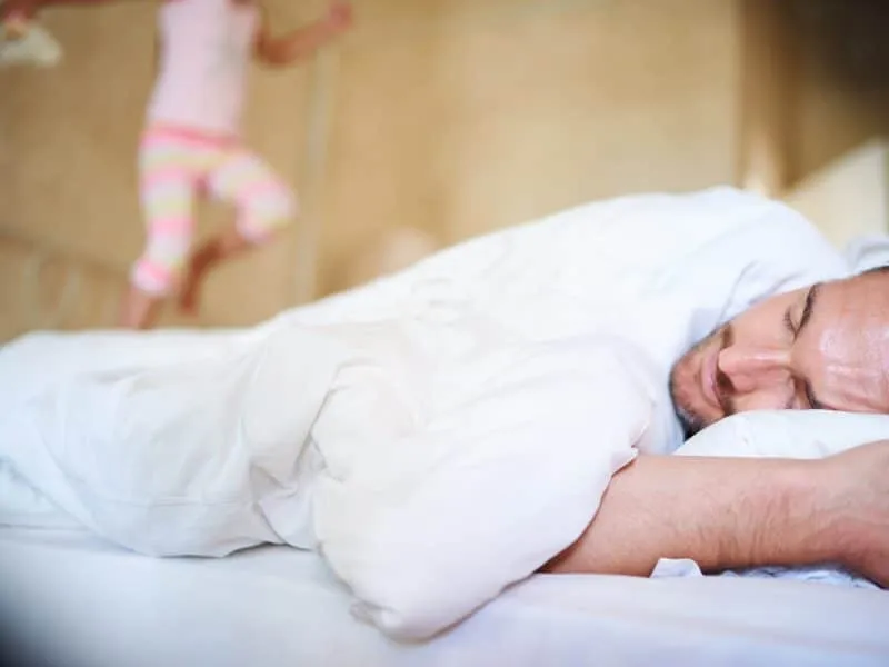 Its morning daddy. Shot of a sleeping dad with his little daughter jumping on the end of the bed