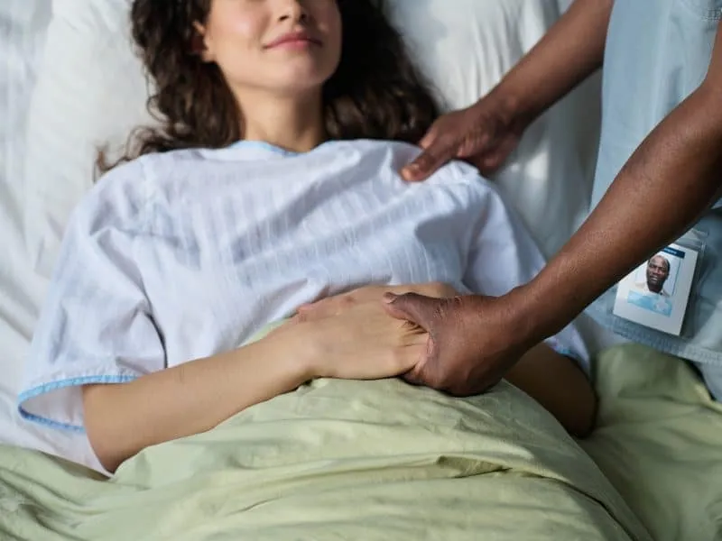 Close-up of male nurse holding hands with patient and supporting her during rehabilitation in hospital ward
