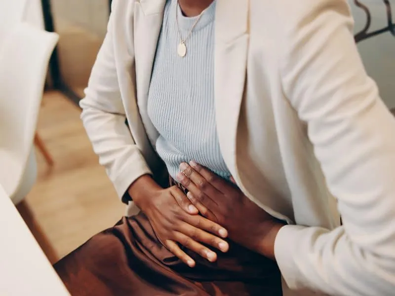 Professional, woman and hands with stomach pain in office for menstrual cramps, constipation and di.