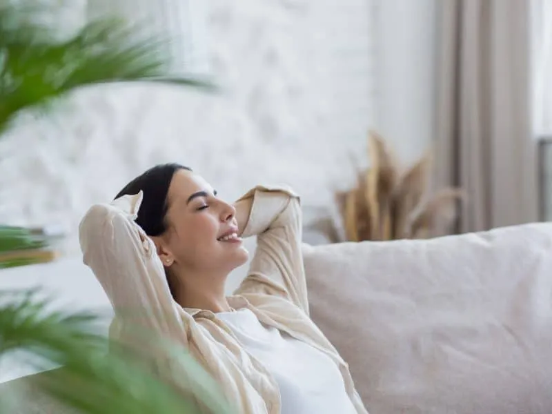 Beautiful brunette woman resting with closed eyes during the day, dreaming and dozing at home sitting on the couch