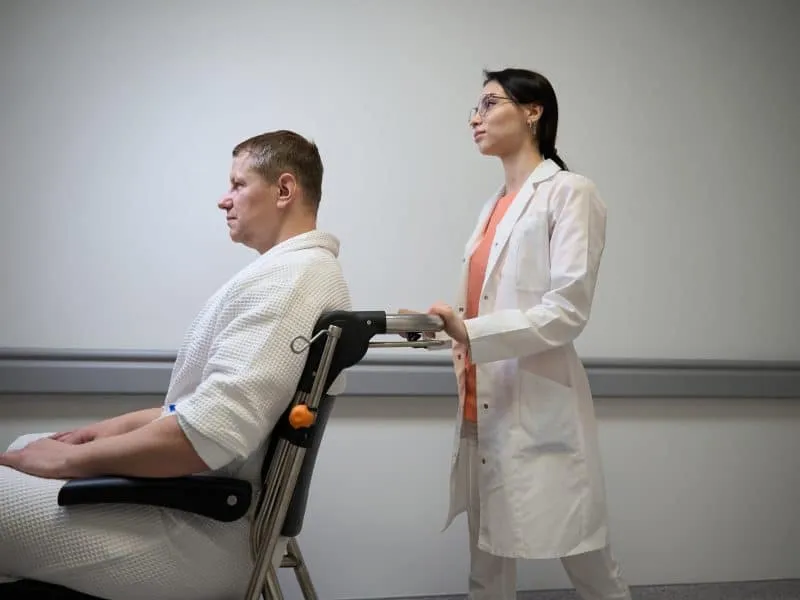 Waist up side view portrait of beautiful qualified nurse is supporting the man on the wheelchair in the hospital