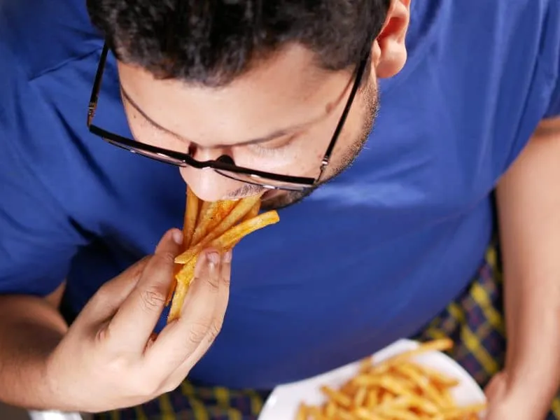 a fat man eating french fries while sited .