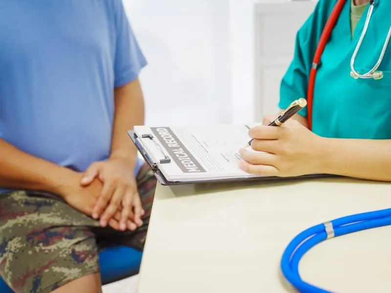 A female doctor sits a hospital desk,examining a sick male patient with hemorrhoid symptoms