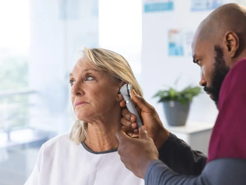 African american male doctor examining senior female caucasian patient using otoscopy. Hospital, work, medicine and healthcare, unaltered.