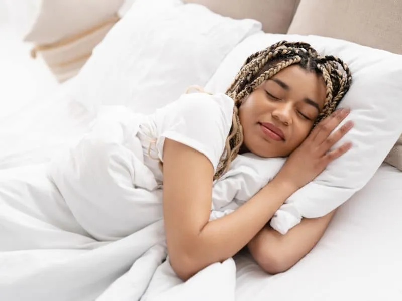 Attractive young african woman sleeping in her bed. Serene calm african american girl sleeping in comfortable bed lying on soft pillow orthopedic mattress. Side view