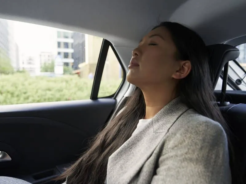 Chinese business woman driving in the car as a passenger with eyes closed